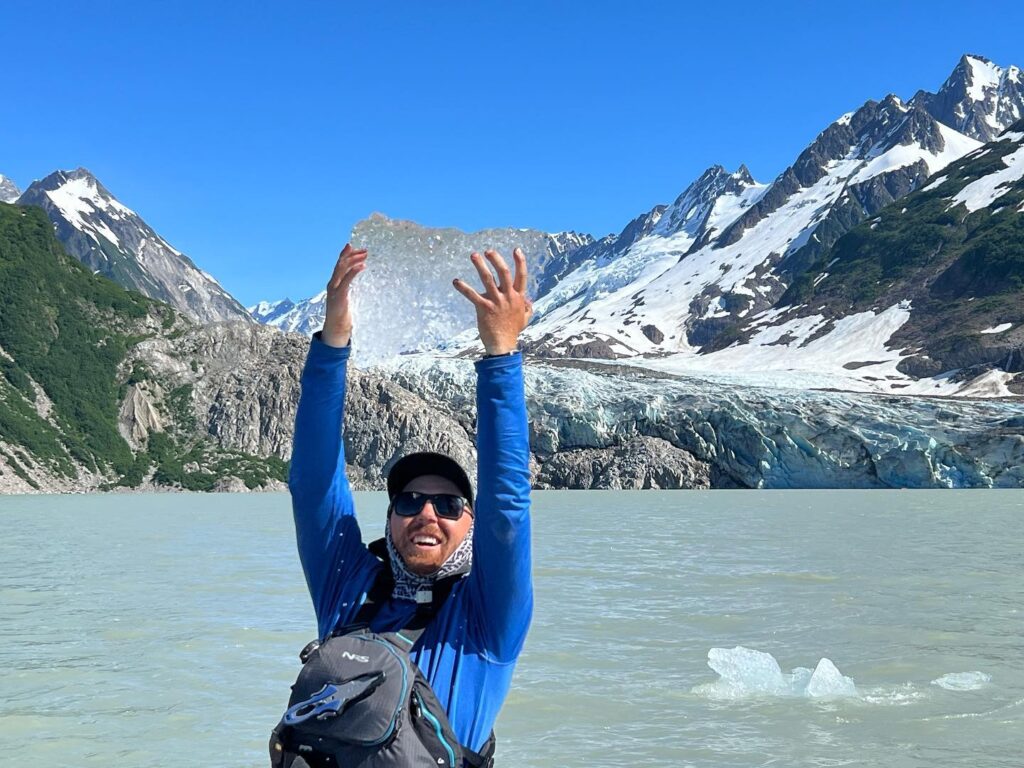 a man holding up a piece of ice in front of a mountain