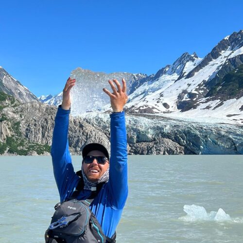 a man holding up a piece of ice in front of a mountain