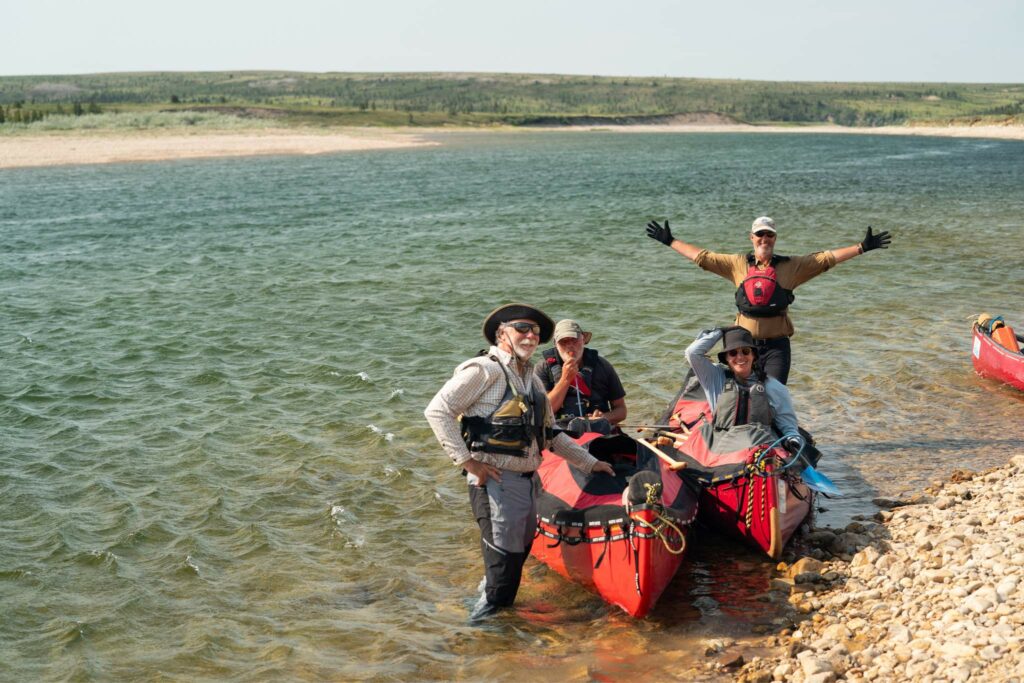a group of people standing on a rocky shore with canoes