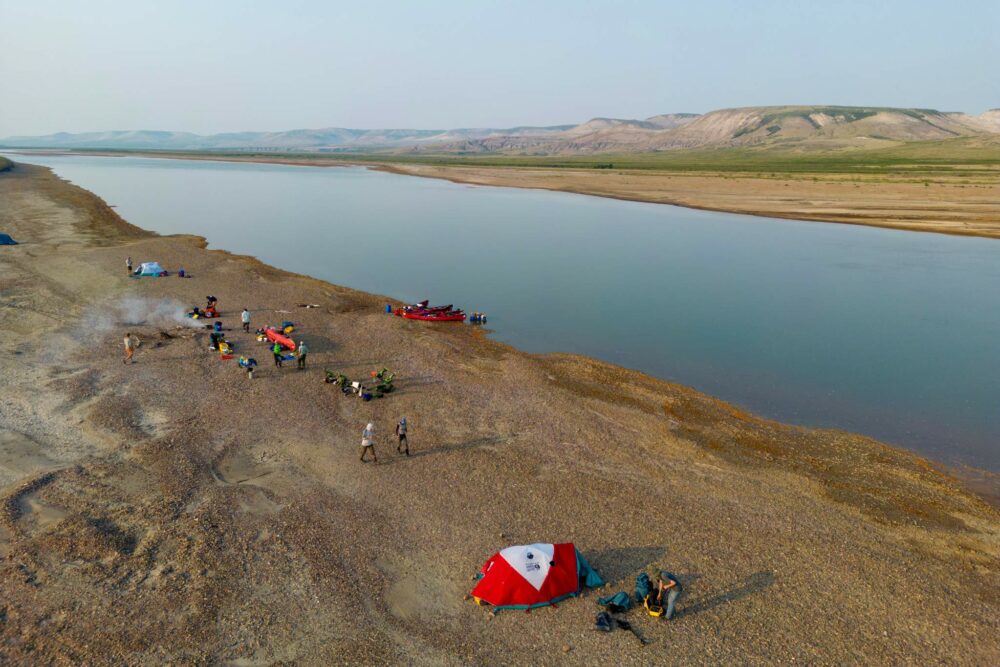 A group of people camped next to the Horton River, as viewed from above by a drone.