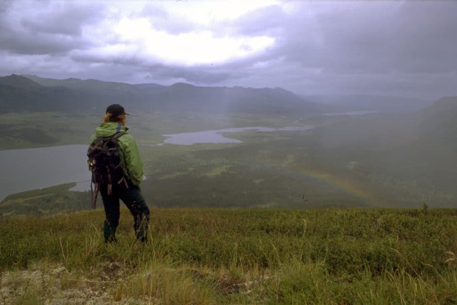 a person standing on a hill looking at a rainbow
