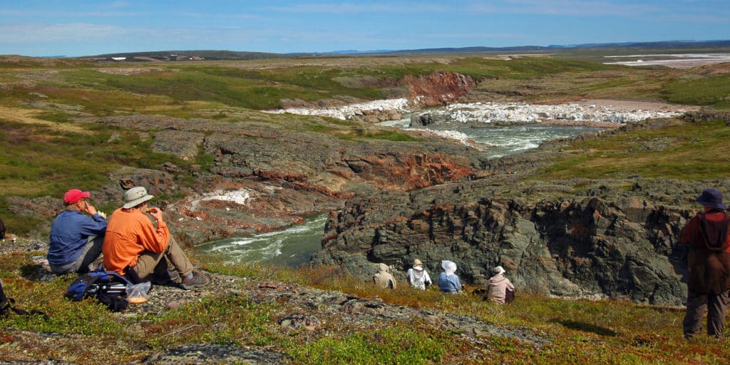 a group of people sitting on a rocky cliff overlooking a river