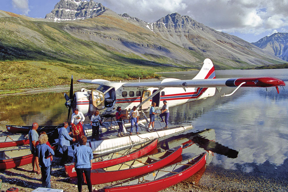Float plane on lake with paddlers unloading canoes and gear in preparation for paddling the Snake River in Yukon, Canada.