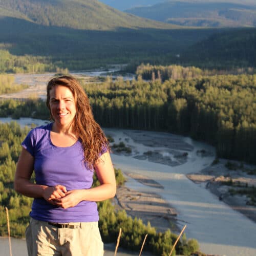 a woman standing on a hill with a river and mountains in the background