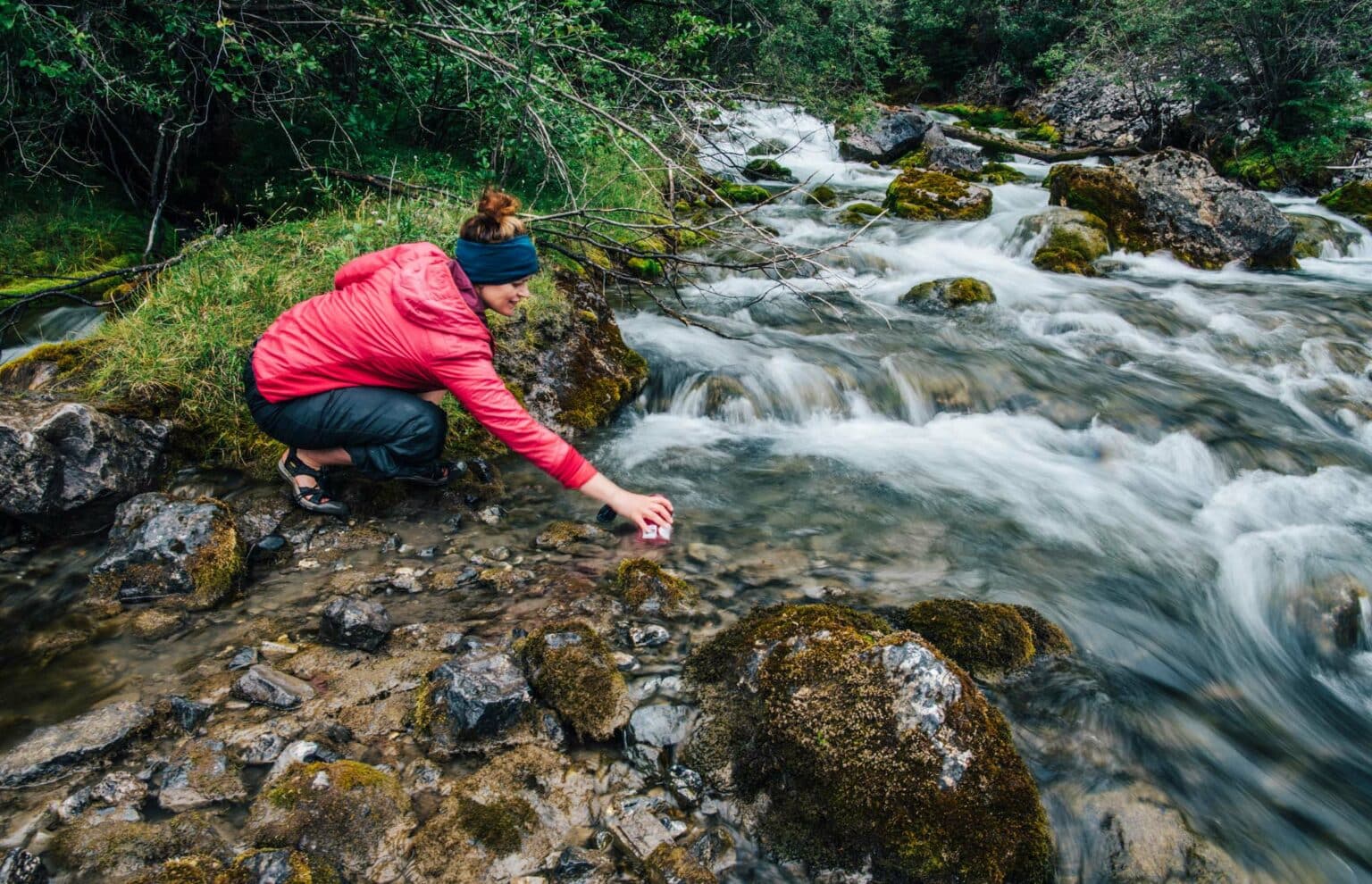 a woman in a red jacket touching rocks in a river