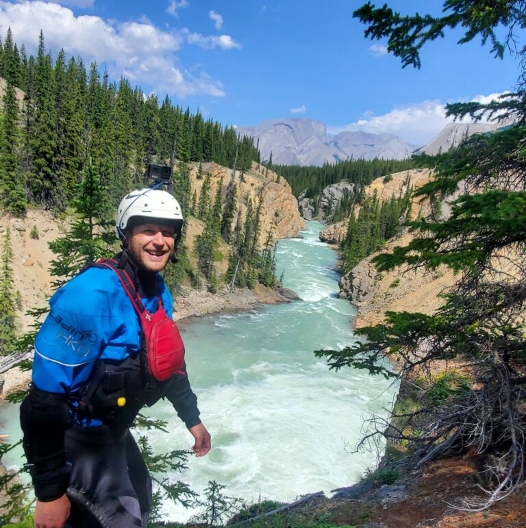 a man wearing a helmet and standing on a cliff near a river