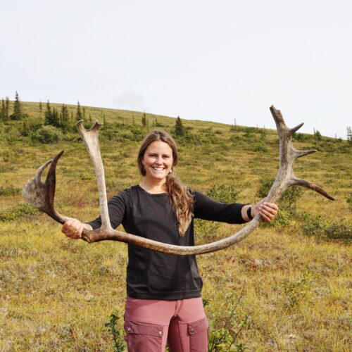 a woman holding up antlers in a field