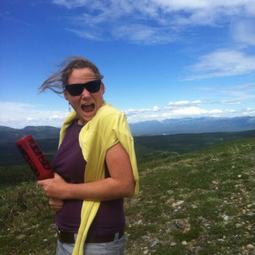 a woman with her mouth open holding a red object on a hill