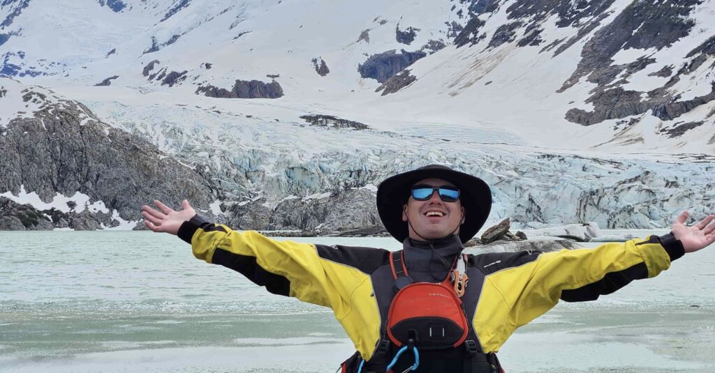 a man in a hat with his arms out in front of a snowy mountain