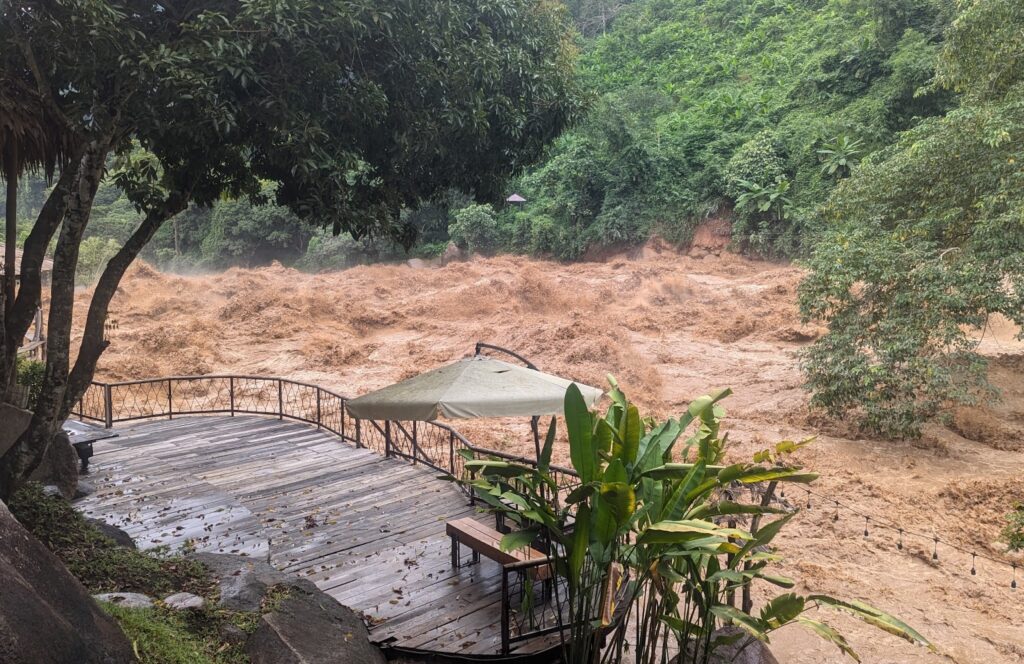 a wooden deck with a bench and umbrella in front of a muddy river