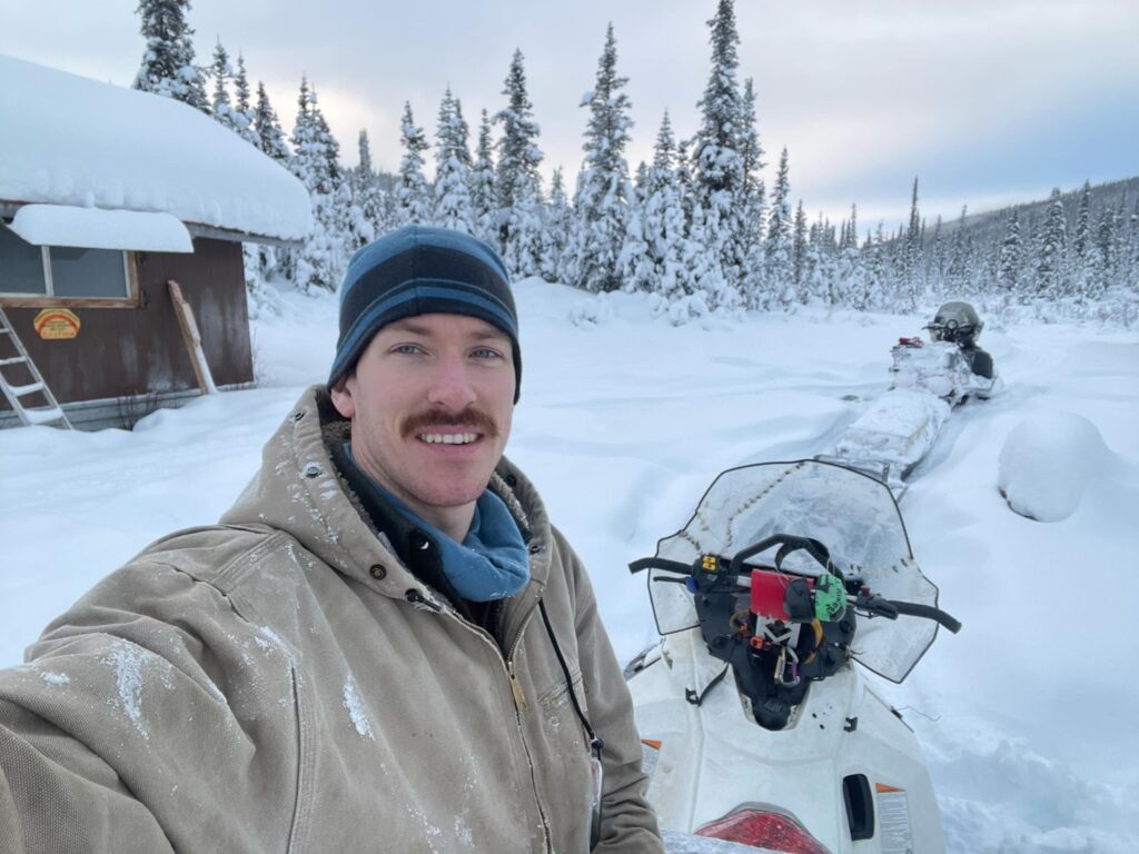 a man taking a selfie with snowmobiles in the snow