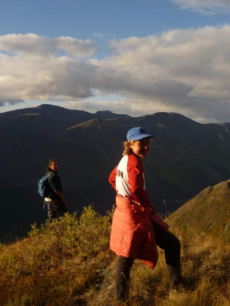 a woman in a red coat and blue hat standing on a mountain