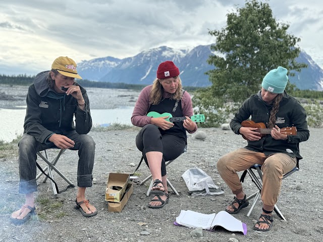 Three people playing ukuleles outdoors