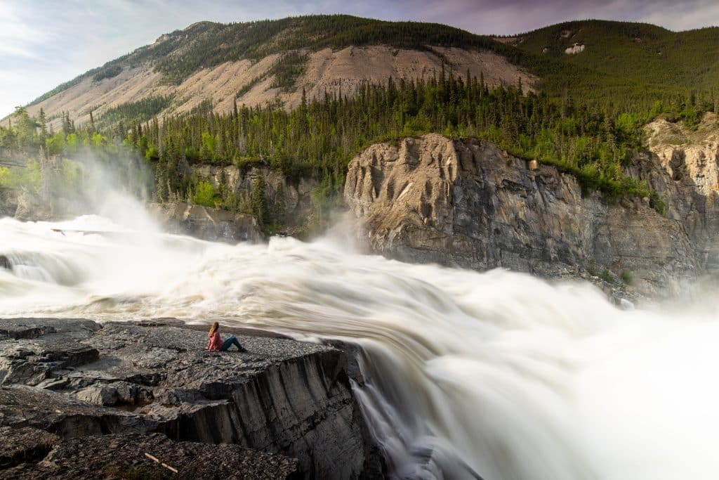 Person sitting by powerful waterfall