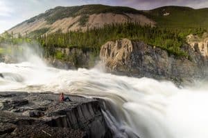Person sitting by powerful waterfall